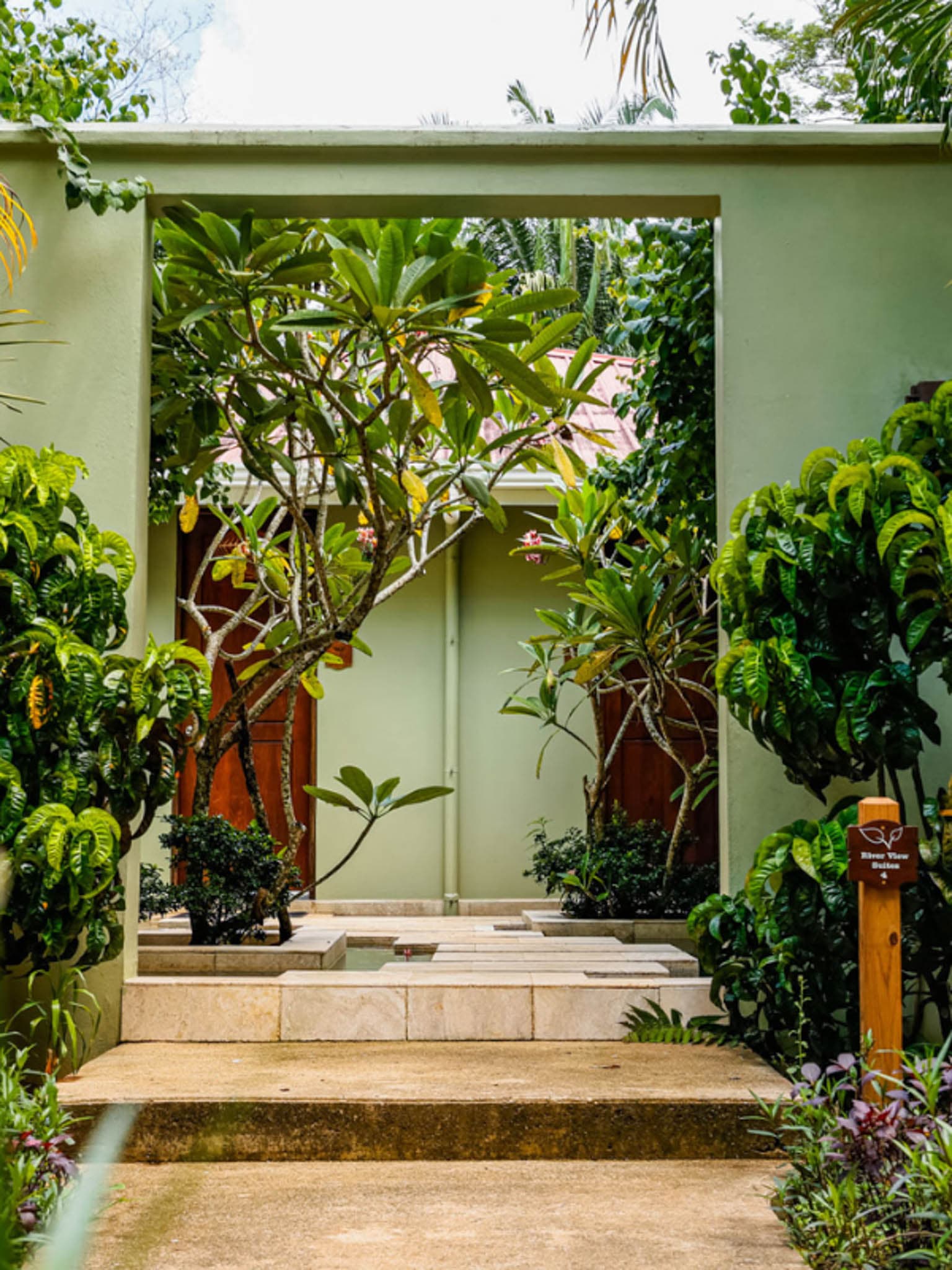 A garden path framed by lush greenery leads to a tranquil courtyard with a stone pathway.