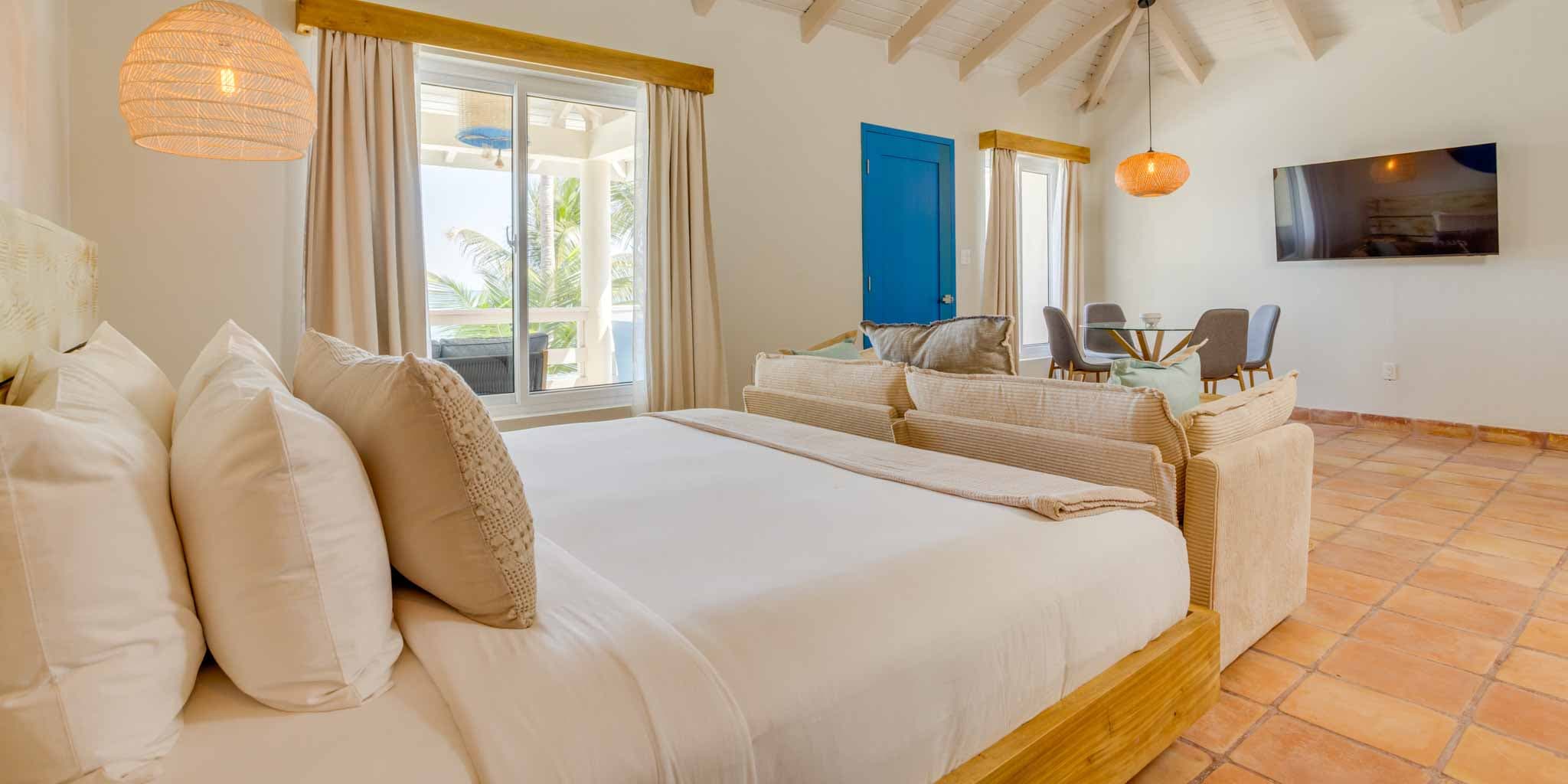A cozy bedroom with a large bed, seating area, and large windows overlooking a patio.