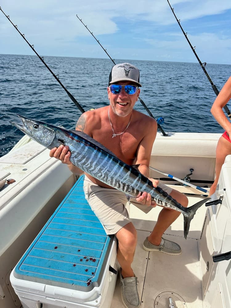 A smiling man holds a large fish while sitting on a fishing boat.