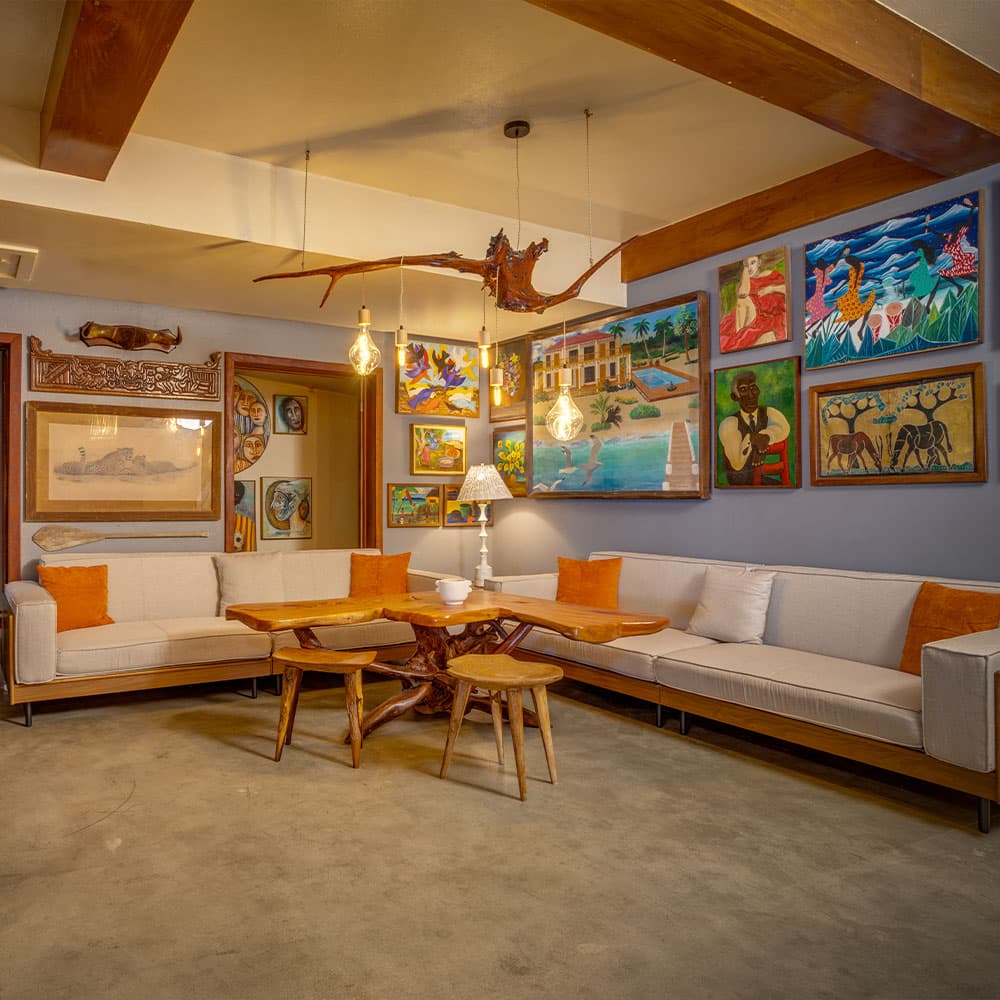 A cozy living room featuring a large wooden table, beige sofas, and colorful artwork on the walls.