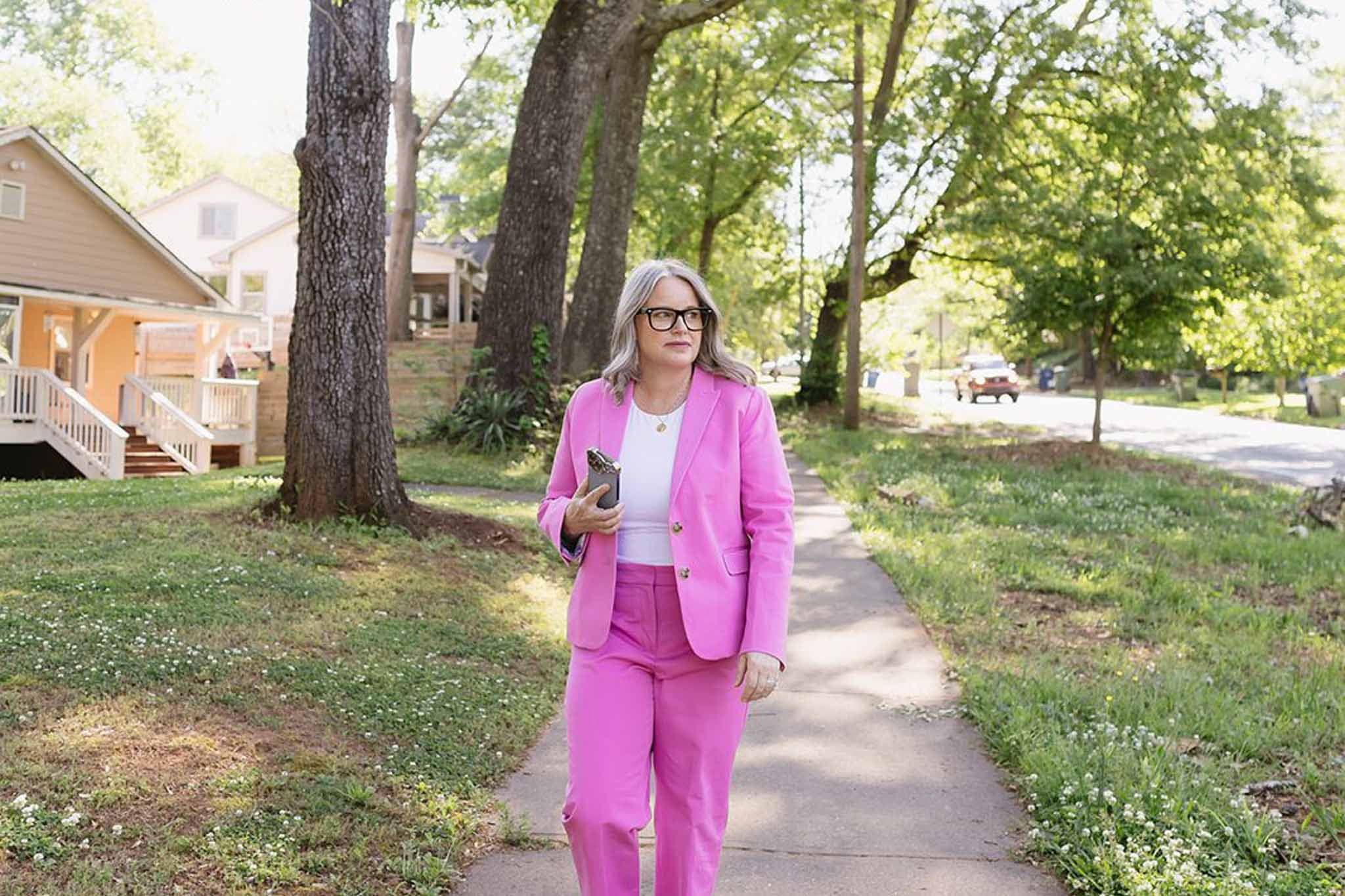 A person wearing a pink suit walks along a sidewalk surrounded by trees and houses.