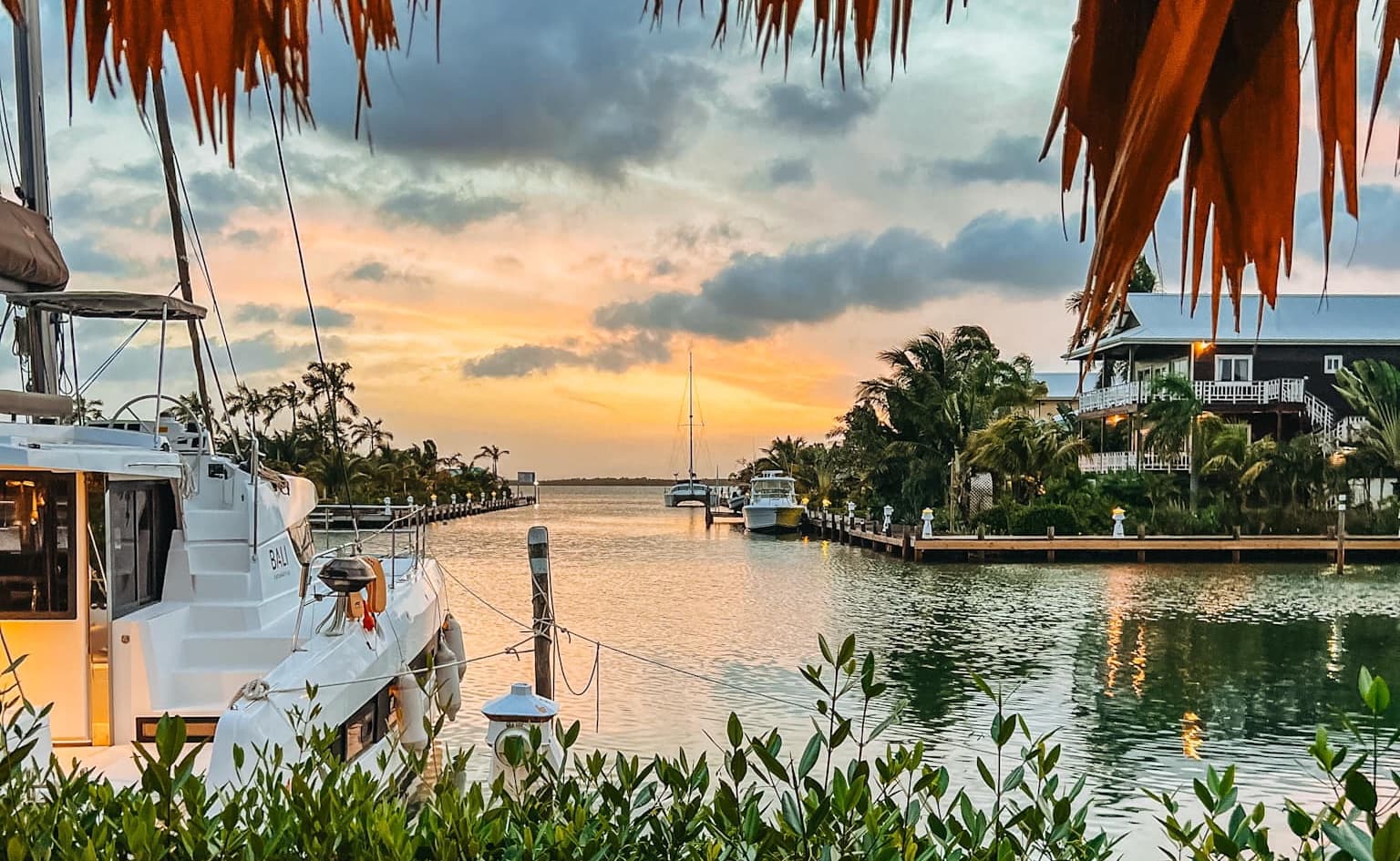 A serene marina at sunset with boats docked and palm trees lining the waterway.