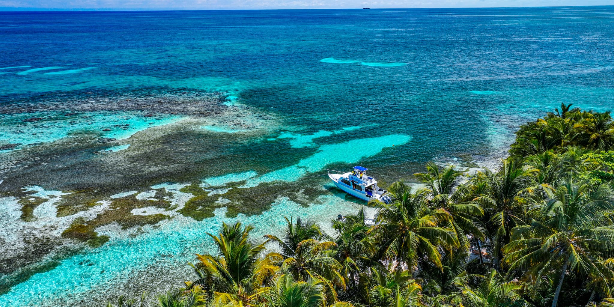 A boat anchored near a tropical shore surrounded by vibrant turquoise waters and lush palm trees.