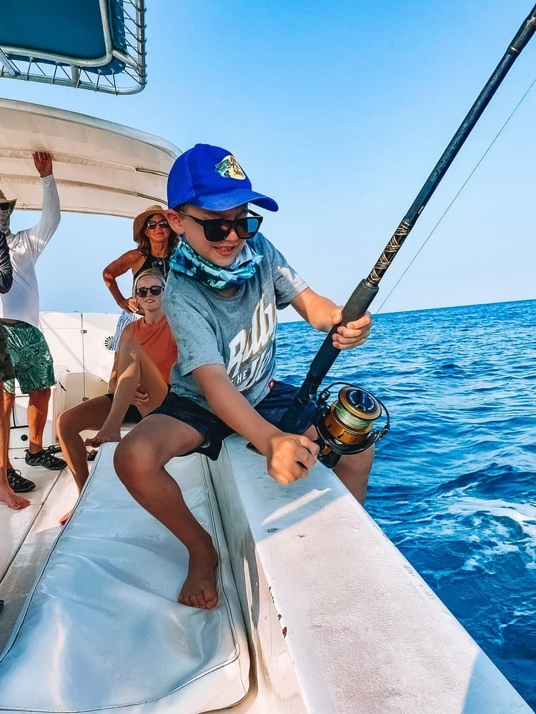 A young boy fishing on a boat, surrounded by family enjoying a day at sea.