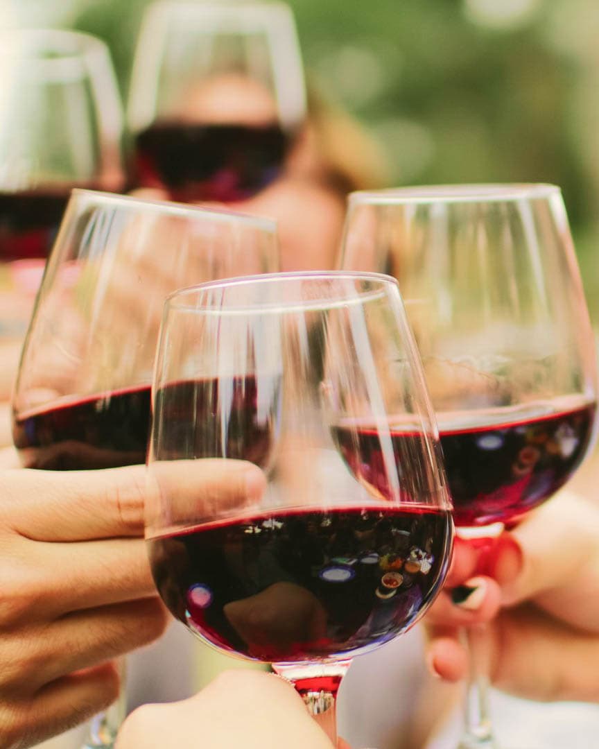 A group of hands toasting with red wine glasses against a blurred background.