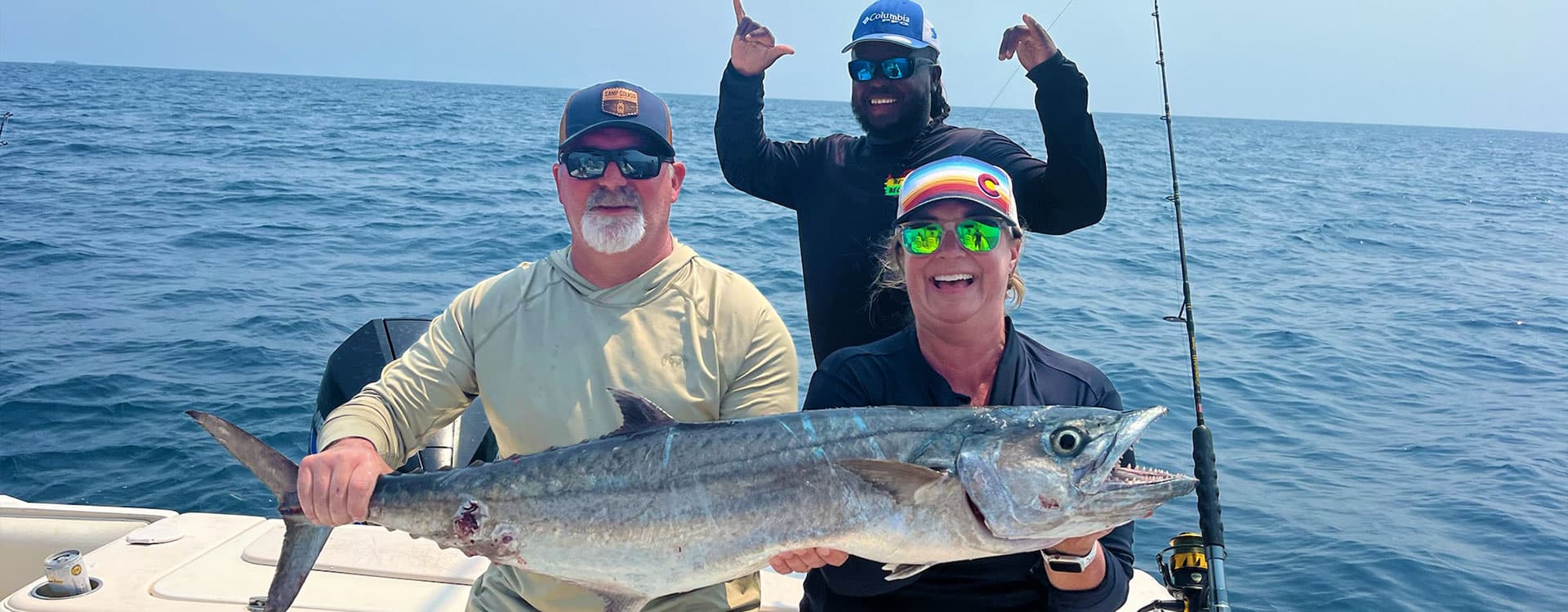 Two fishermen proudly display a large fish while a third man celebrates behind them on a boat.