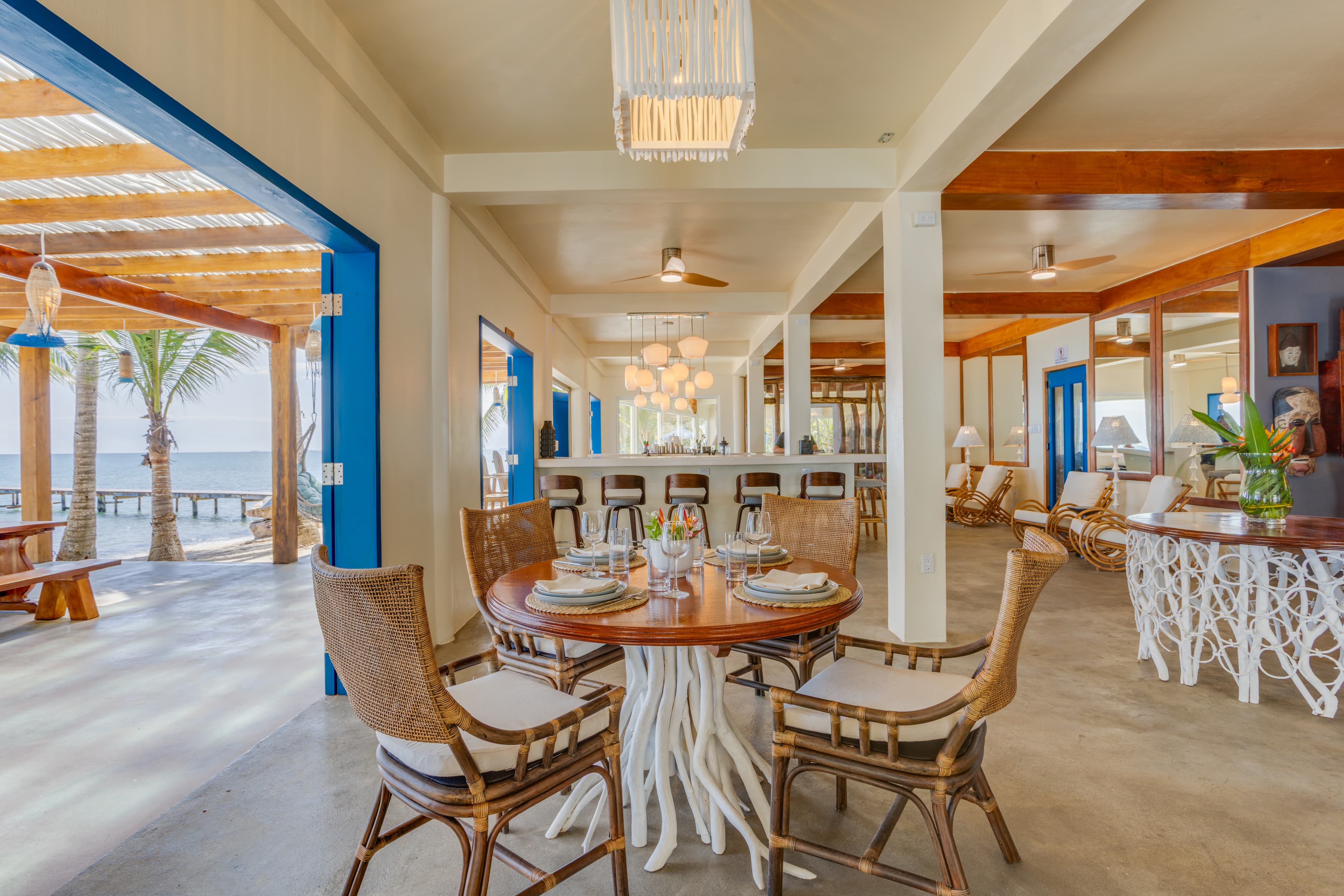 A bright, modern dining area featuring a round wooden table and open views of the sea.
