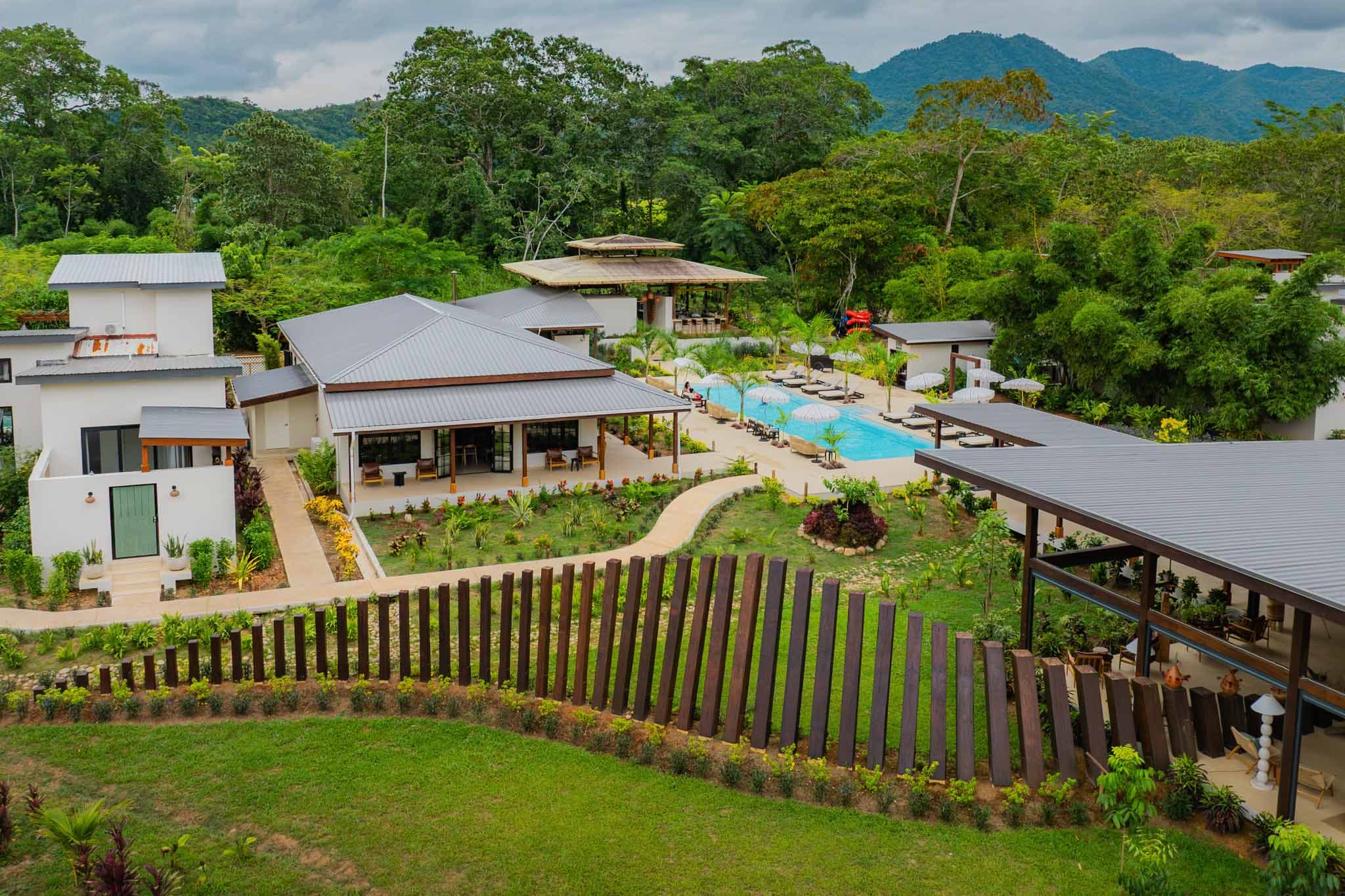 A lush resort featuring modern buildings, a swimming pool, and landscaped gardens surrounded by mountains.