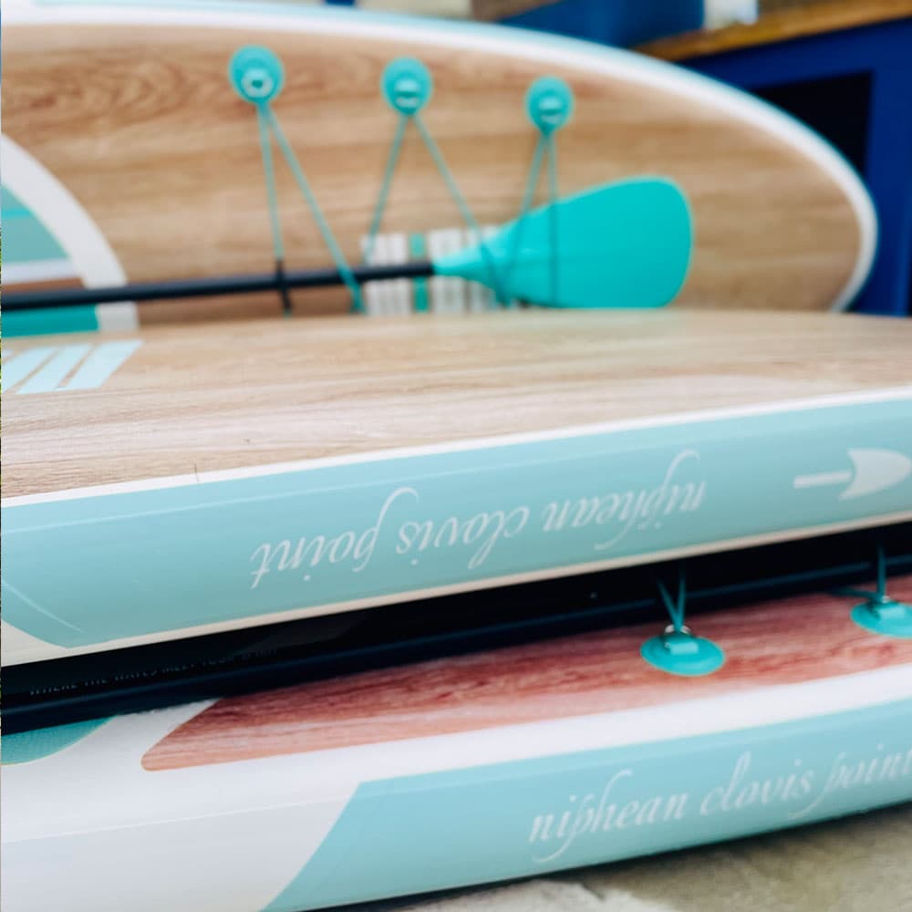 Close-up of two paddleboards stacked together, featuring a wooden finish and turquoise details.