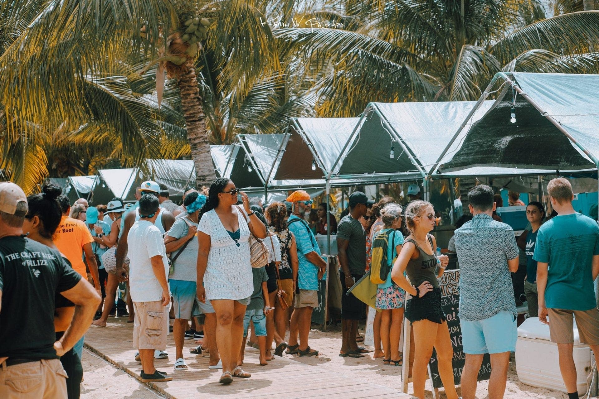 Crowds of people browse market stalls under palm trees.