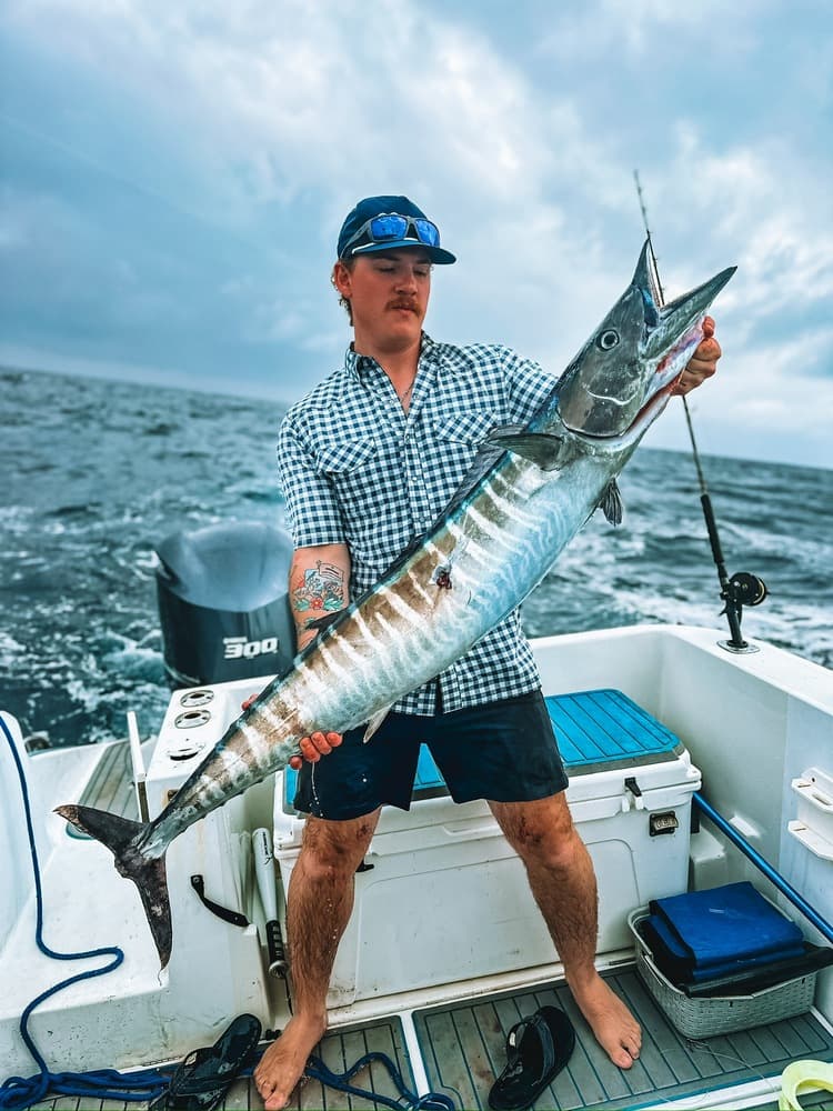 A person in a plaid shirt holds a large fish on a boat at sea.