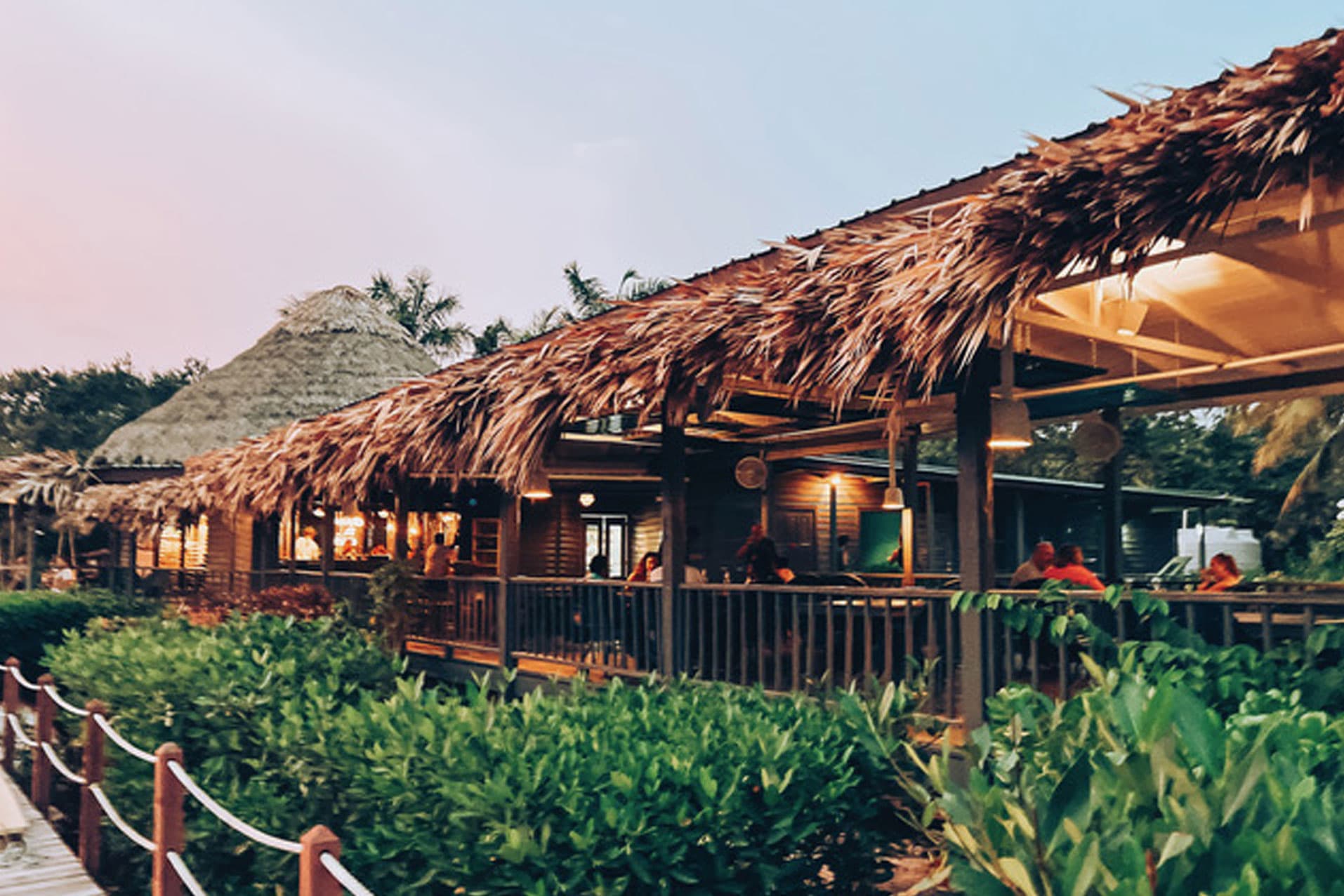 A tropical restaurant with thatched roofs and outdoor seating surrounded by greenery.