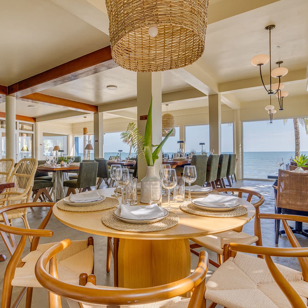 A stylish seaside restaurant interior featuring a round wooden table set for dining.