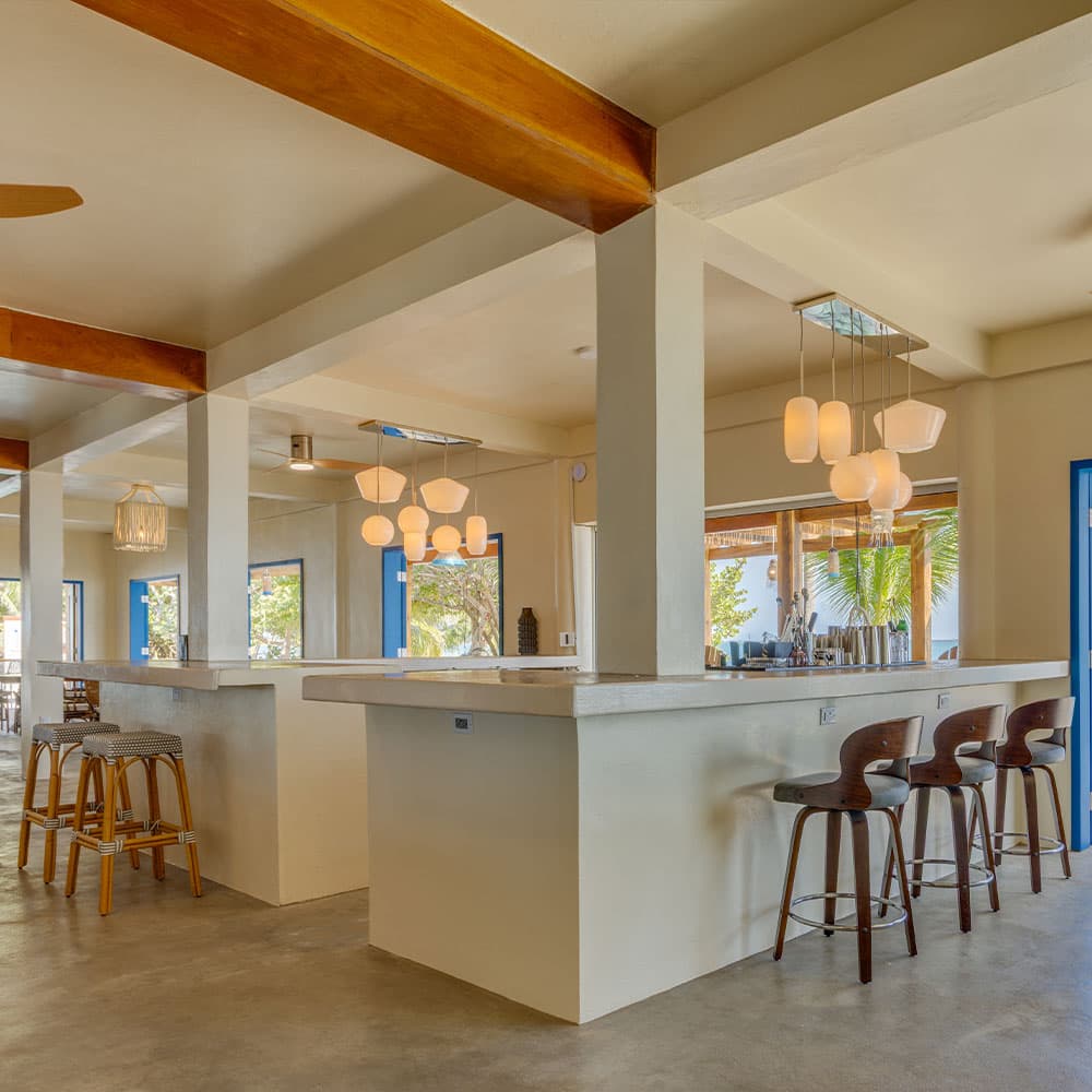 A modern bar area with wooden beams and soft lighting, featuring a minimalist design and empty stools.