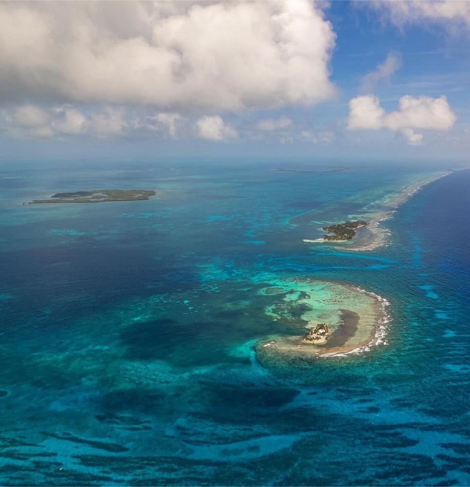 Aerial view of a turquoise coastline with small islands and clouds overhead.
