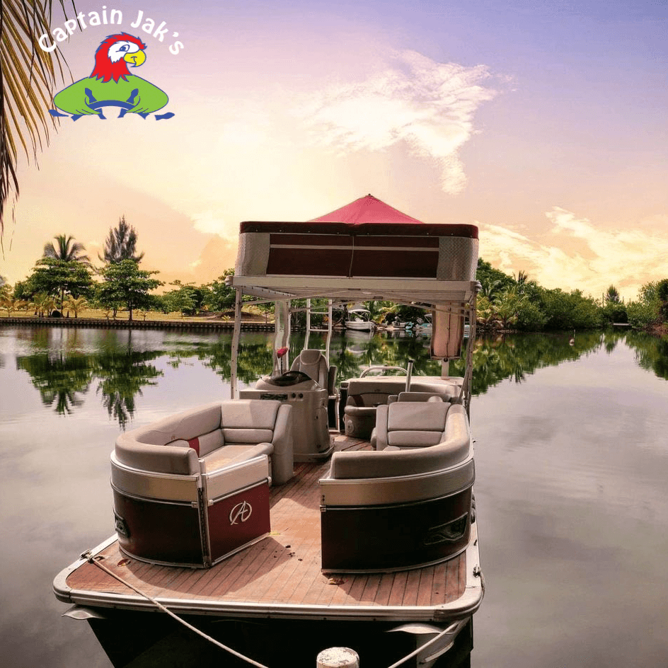 A cozy pontoon boat is moored by a tranquil lake at sunset, surrounded by lush greenery.