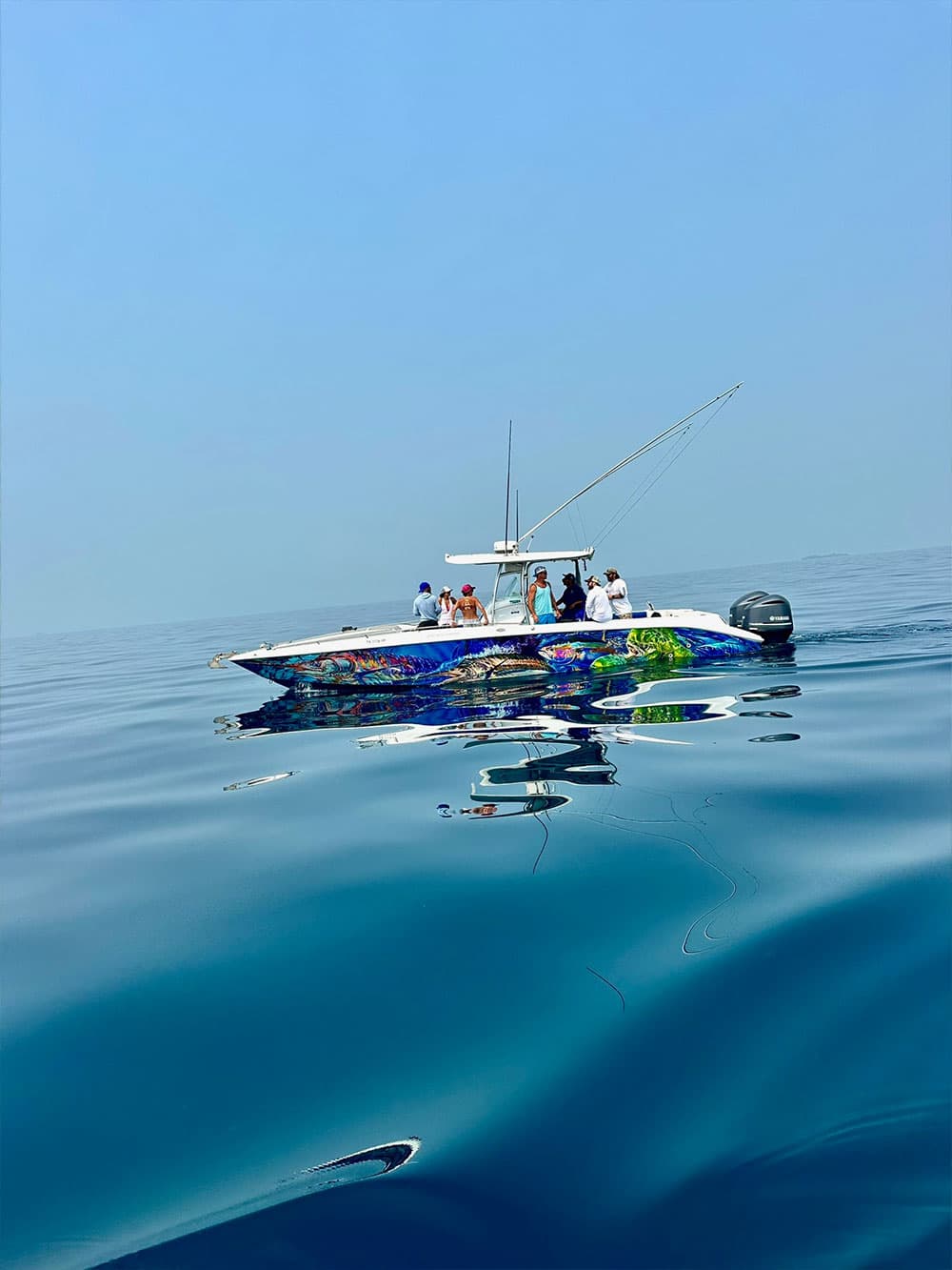A colorful boat with several people is floating on calm blue waters under a clear sky.