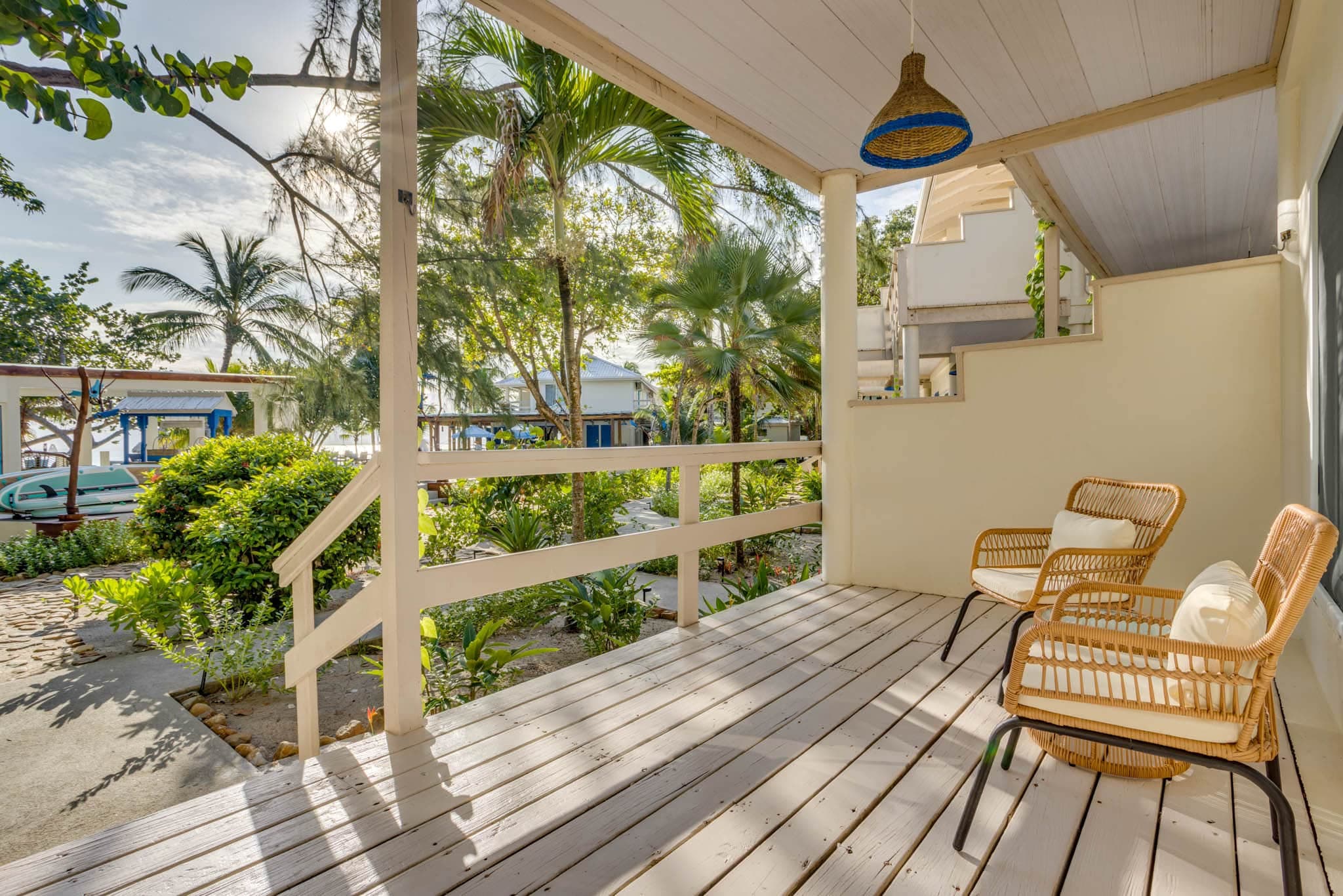 A serene outdoor porch with two wicker chairs, surrounded by lush greenery and palm trees.