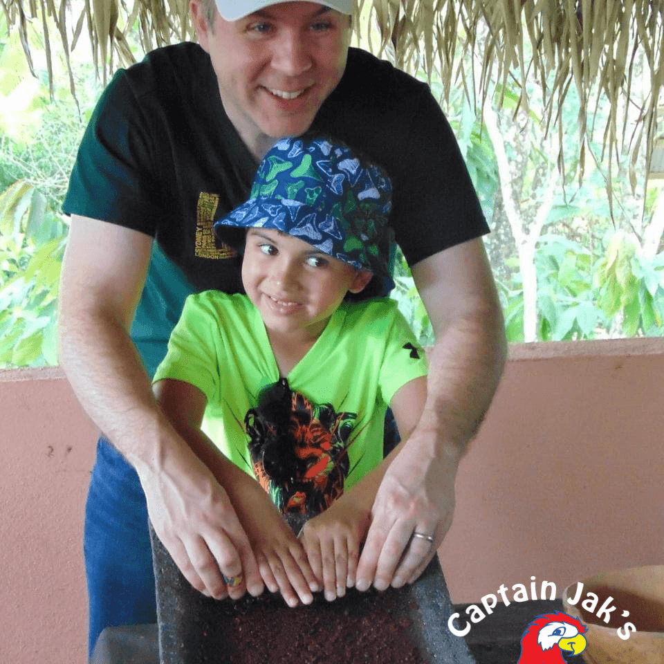A man and a boy smile together while placing their hands on a textured surface in a lush outdoor setting.