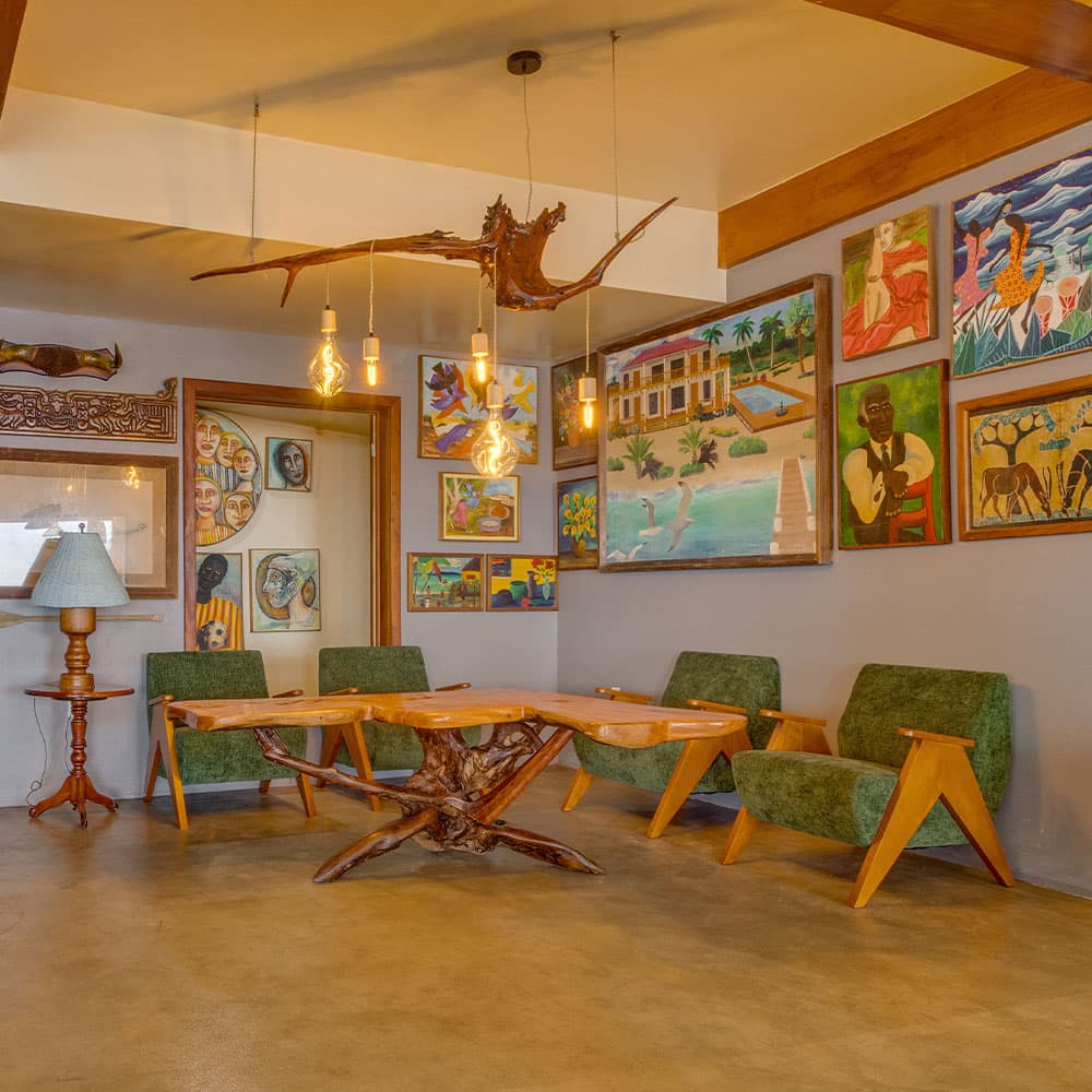 A cozy seating area featuring green chairs, a wooden table, and vibrant artwork on the walls.