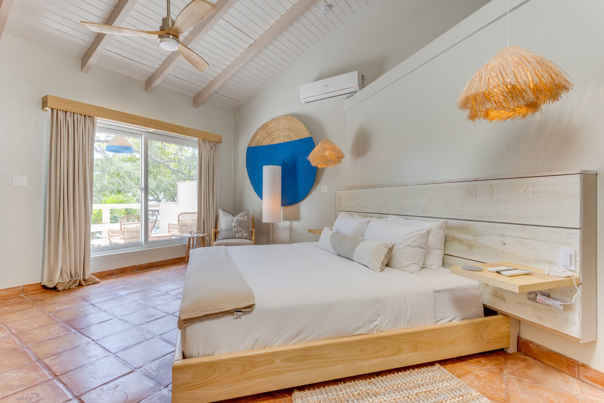Bright and airy bedroom with a wooden bed, decorative lighting, and large windows opening to a patio.