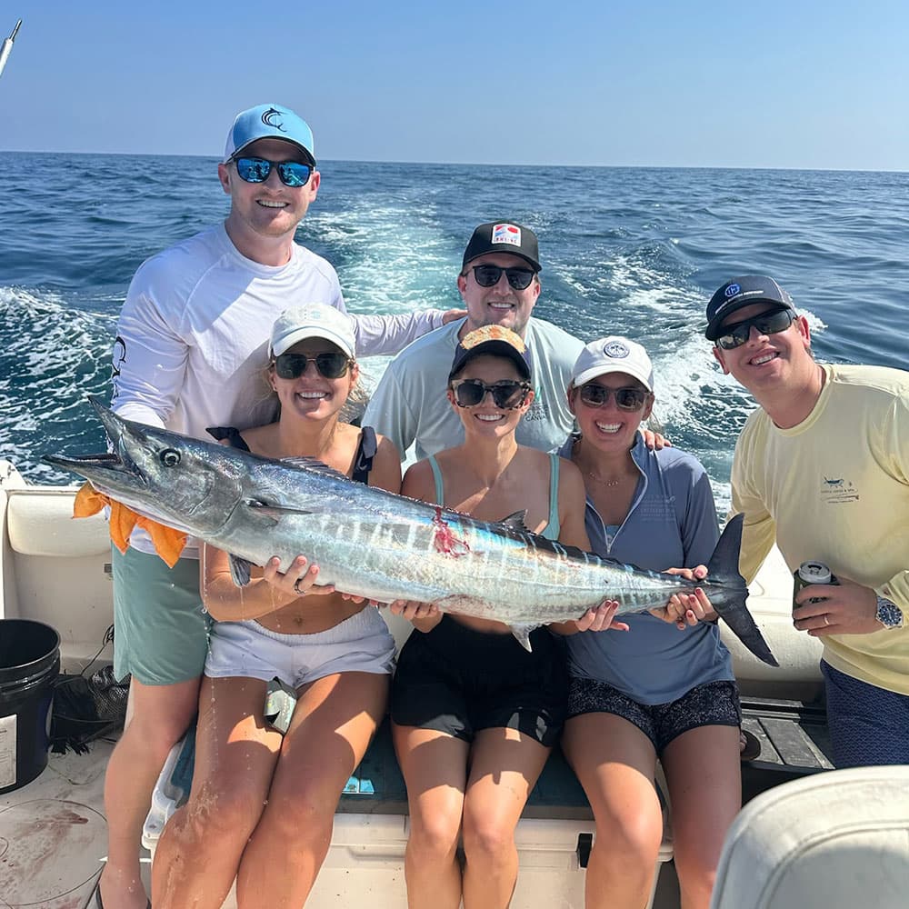 A group of six people on a boat proudly displays a large fish they caught while fishing at sea.