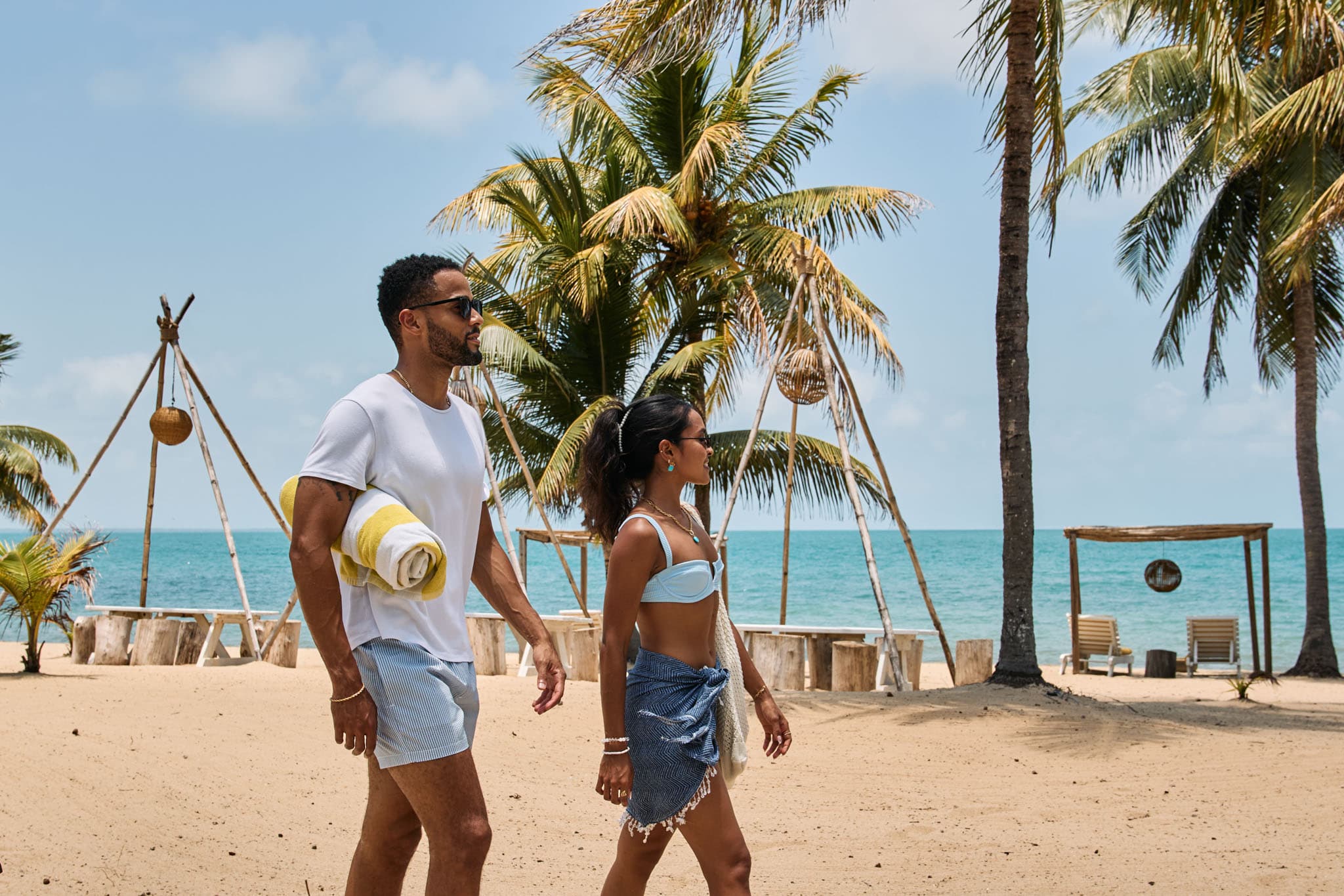 A couple strolls along a sandy beach lined with palm trees and ocean views.