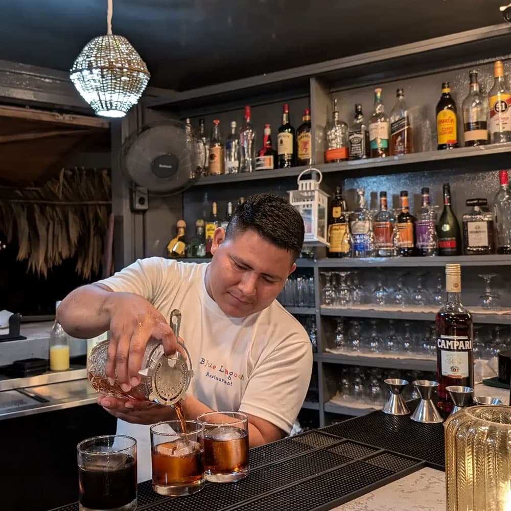 A bartender pours drinks at a bar counter filled with various bottles of alcohol.