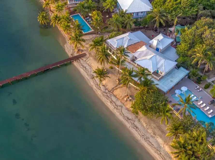 Aerial view of Blue Reef Beach Resort showing the pool, blue roofs, and private dock extending into the Caribbean Sea