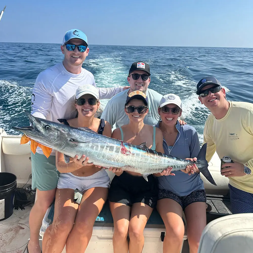 Des personnes heureuses montrant une grosse prise de barracuda sur un bateau en mouvement avec l'eau de l'océan qui défile