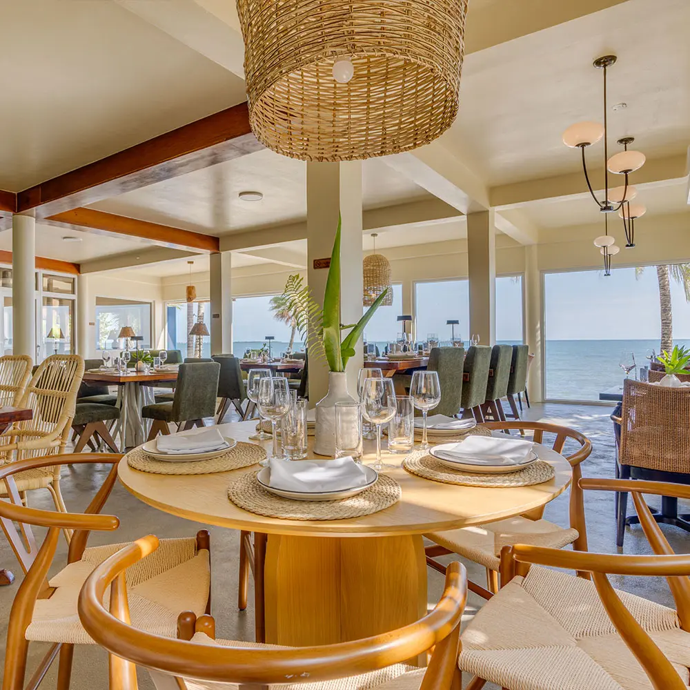 Comedor interior con aire acondicionado y una mesa junto a amplios ventanales con vistas al mar
