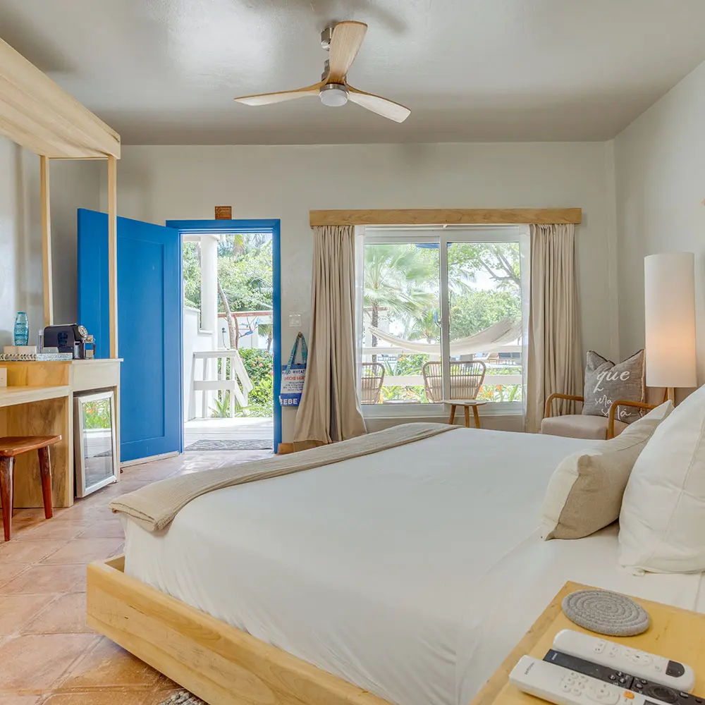 Interior de um quarto no térreo do Blue Reef Beach Resort mostrando uma cama, paredes brancas, uma porta azul e janelas de vidro com vista para a piscina