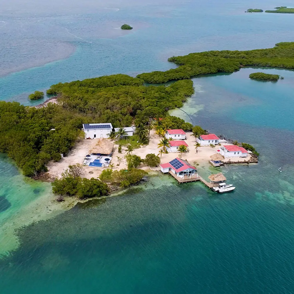 Vista de drone do resort ecológico Blue Reef Island apresentando cabanas, um píer e um restaurante com painéis solares